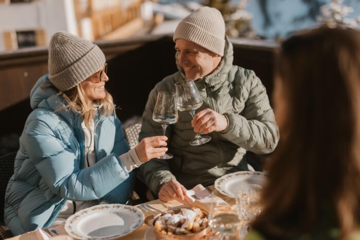 zwei Personen genießen ihren Skitag auf der Sonnenterrasse in Lech Zürs am Arlberg mit einem Glas Weißwein