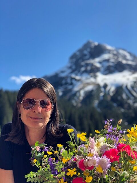 Frau lächelt mit Blumenstrauss und Bergpanorama im Hintergrund