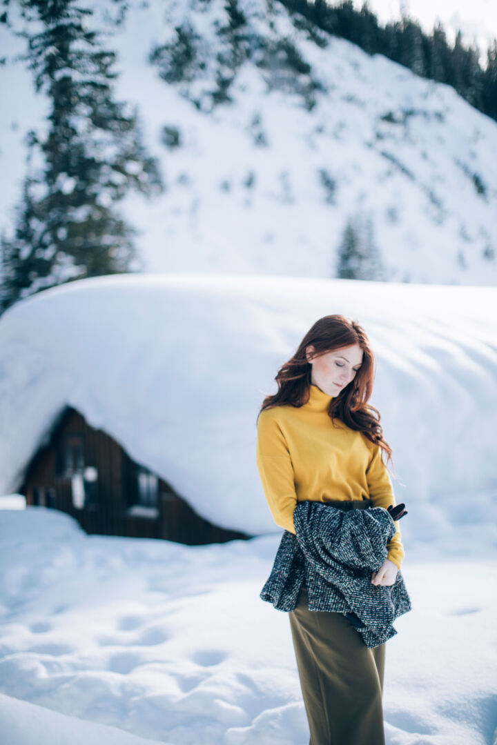eine Frau steht inmitten der Schneelandschaft im Hintergrund sieht man den verschneiten Winterwald und die Holzhütte