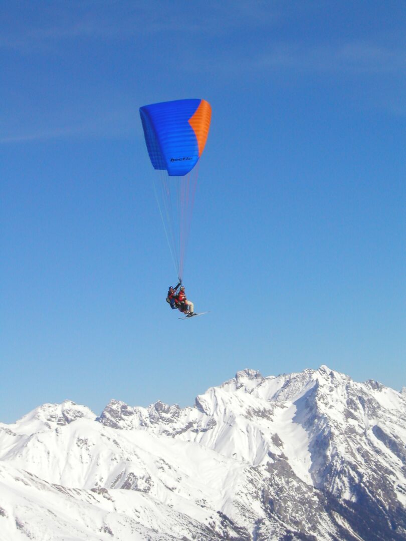 Gleitschirmflieger im Tandem vor strahlend blauem Himmel und darunter die Berggipfellandschaft 
