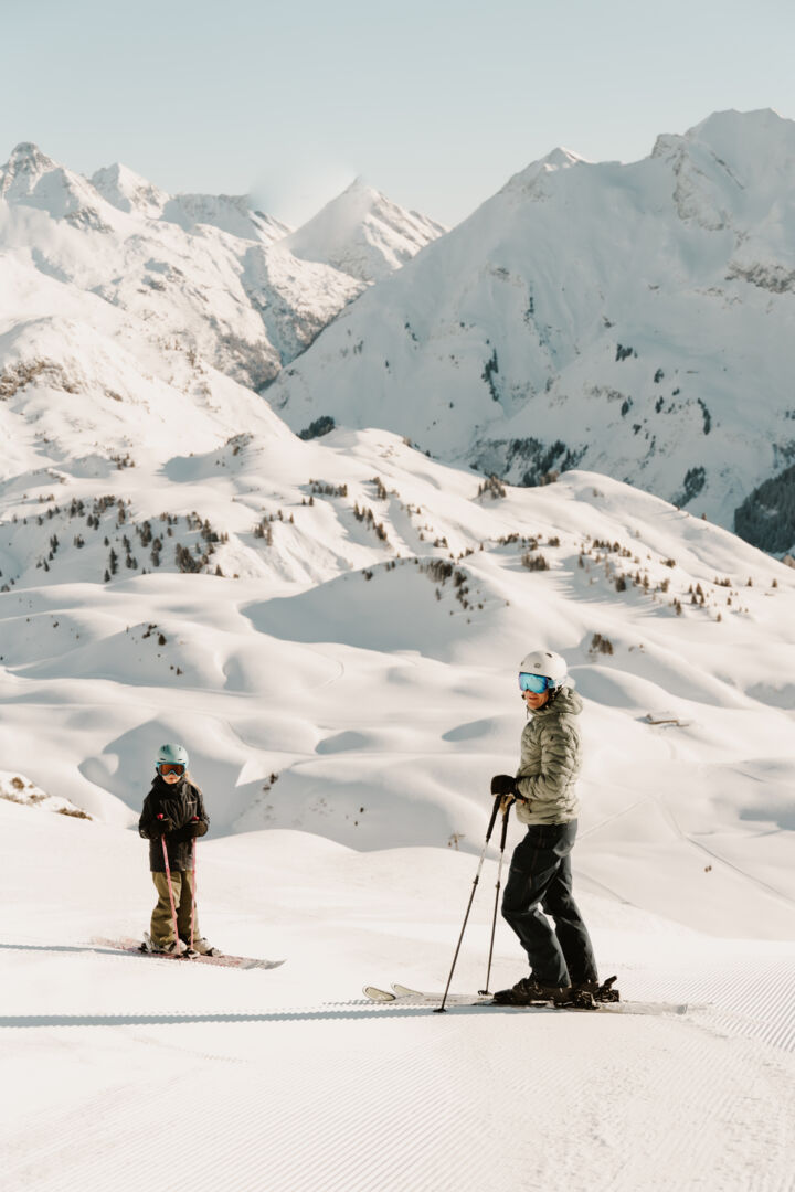 Vater mit Kind stehen auf der Piste mit Blick aufs Panorama