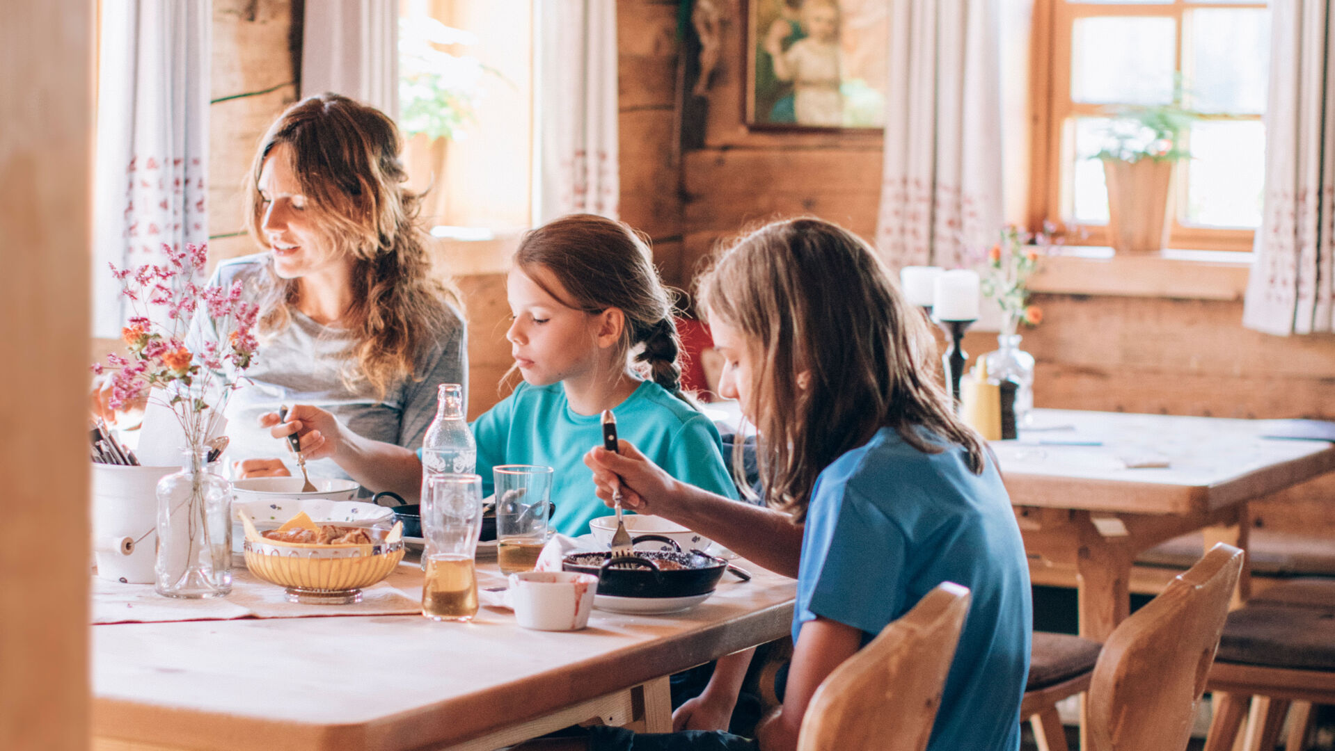 Eine Mutter sitzt mit ihren zwei Töchtern in einer Hütte am Tisch und alle zusammen essen
