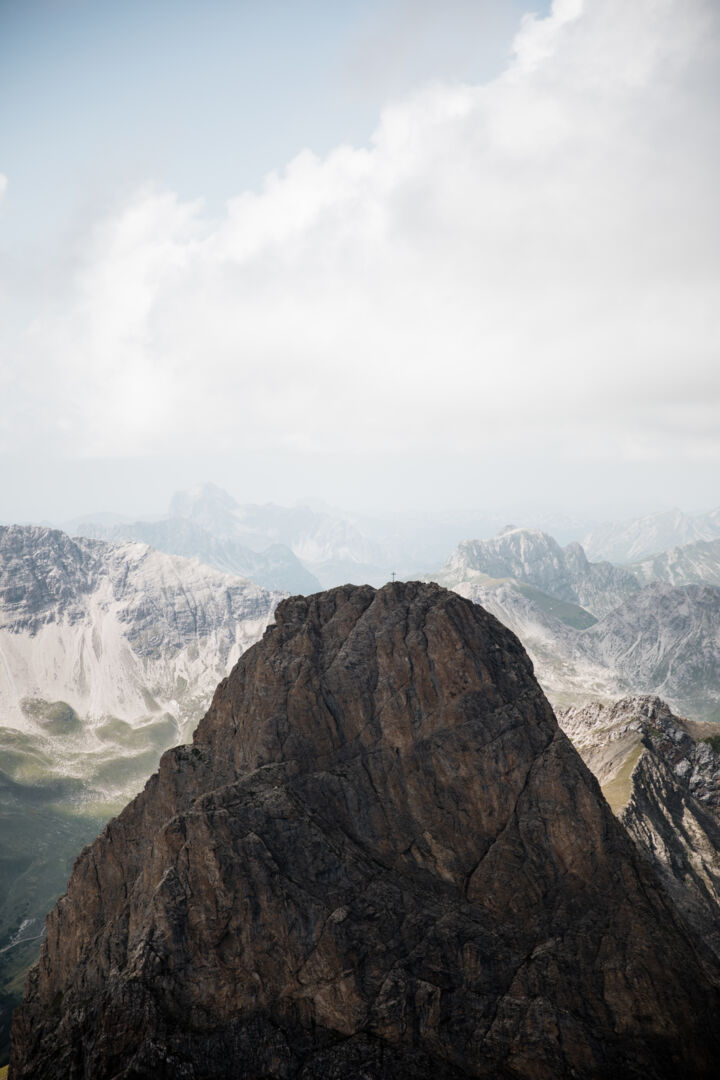 Gipfelkreuz auf einem schroffen Felsgipfel, im Hintergrund weitere Berge im Dunst.
