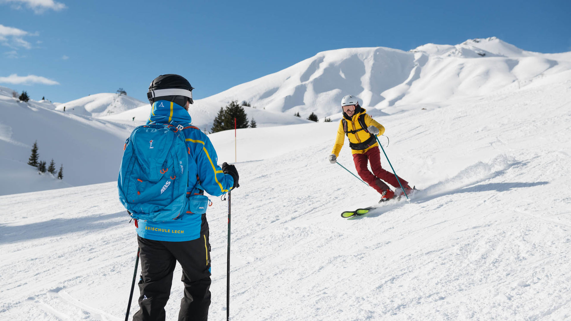 zwei Skifahrer fahren über die Piste in Lech und im Hintergrund sieht man die traumhafte Winterlandschaft