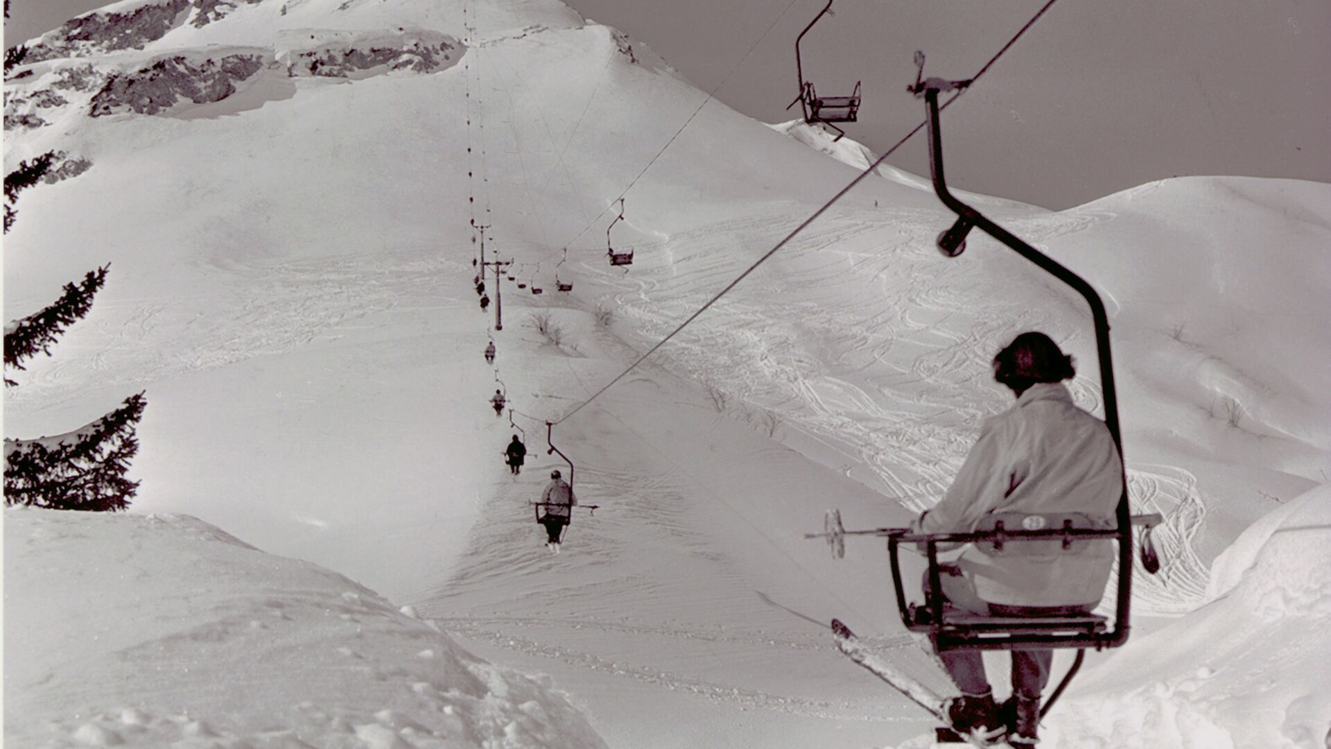 Blick auf eine Person die in einem alten Sessellift in Lech Zürs auf den Berg hochfährt im Winter