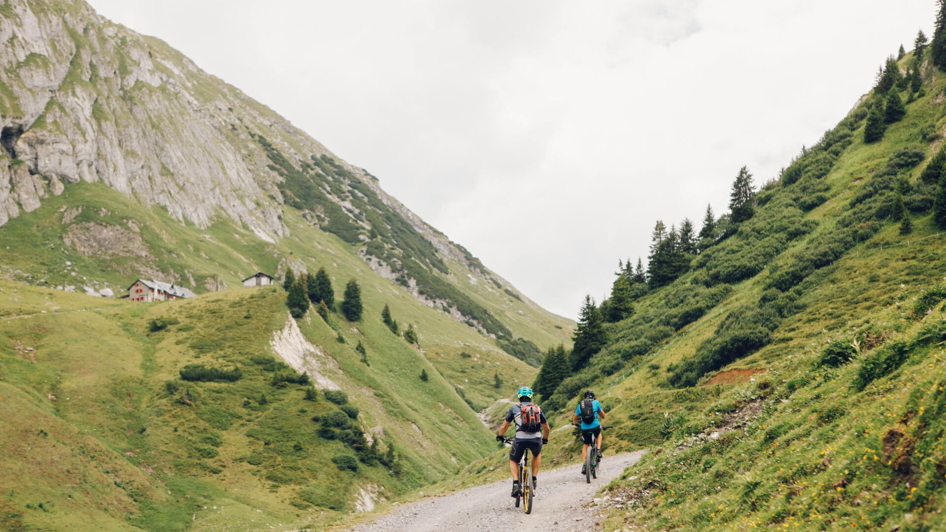 Zwei Radfahrer fahren auf einem Schotterweg durch ein Tal in den Bergen.