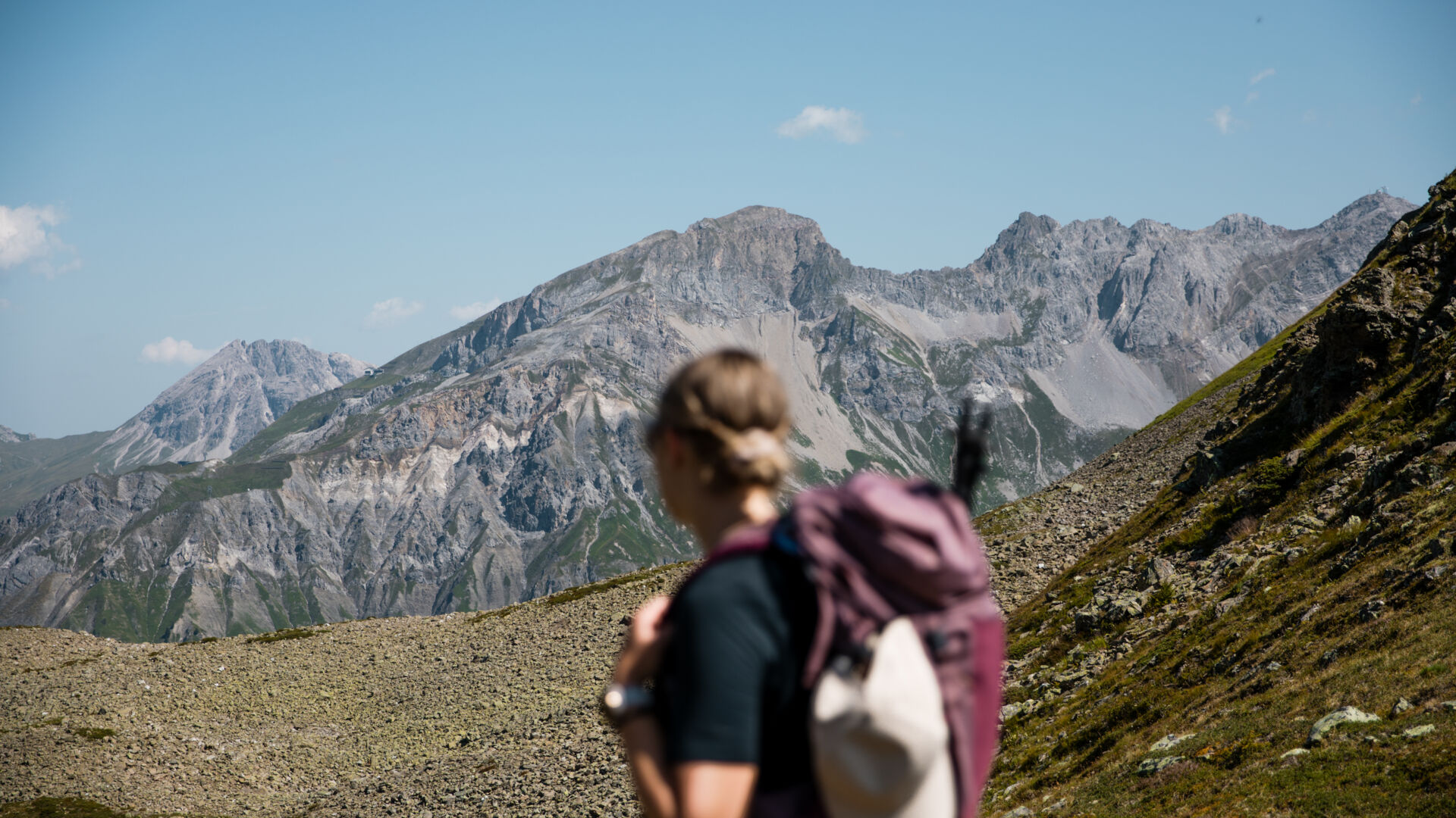Trailrunnerin mit Rucksack auf einem alpinen Wanderweg vor der beeindruckenden Bergkulisse des Arlbergs.