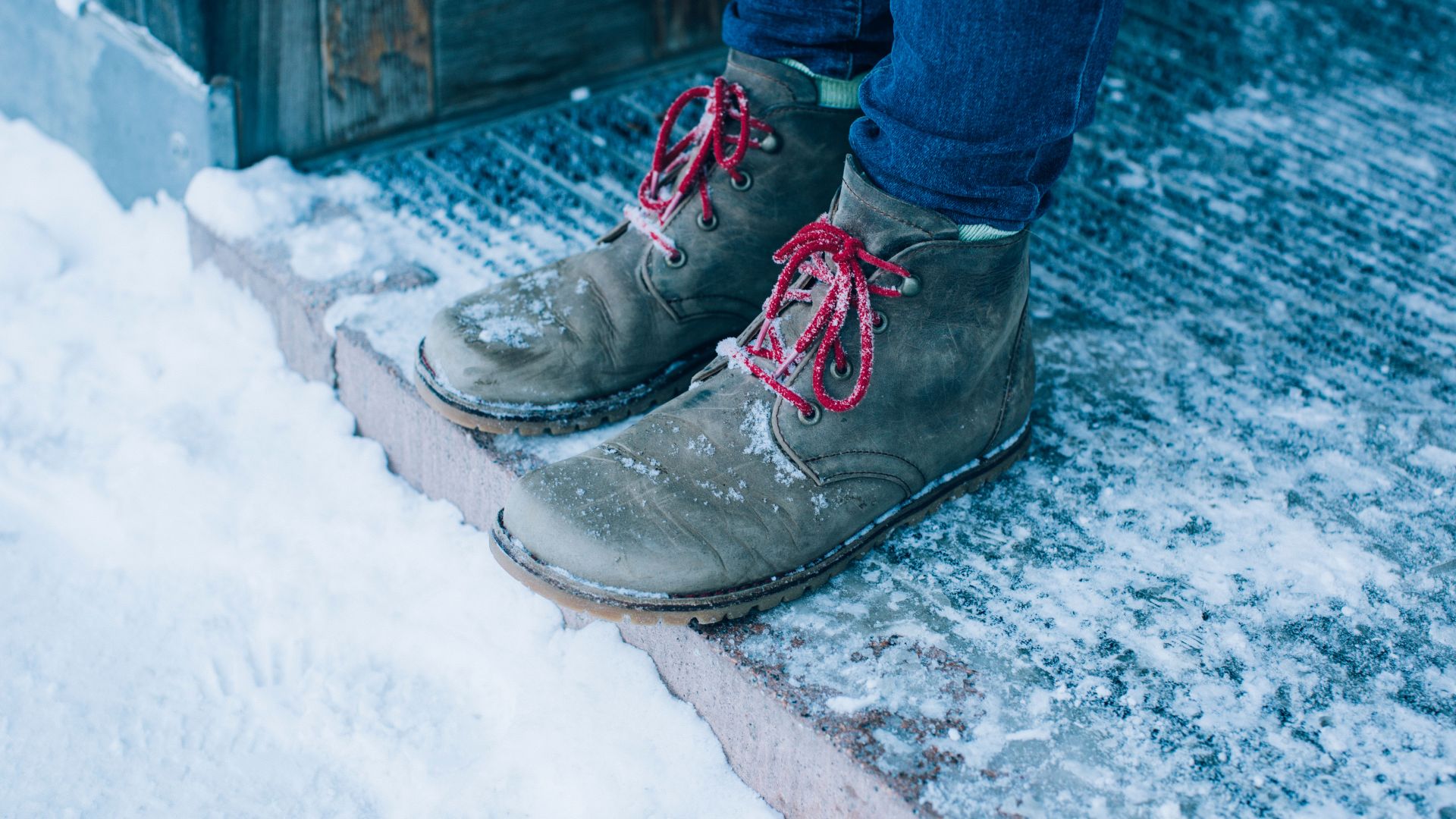 Blick auf die Füße einer Person wie sie im Eingangsbereich steht und der Boden mit Schnee bedeckt ist