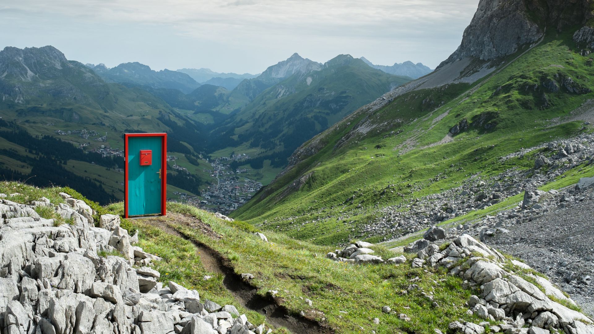 Eine rot-türkise Tür steht inmitten der Berge an der Strecke des Grünen Rings