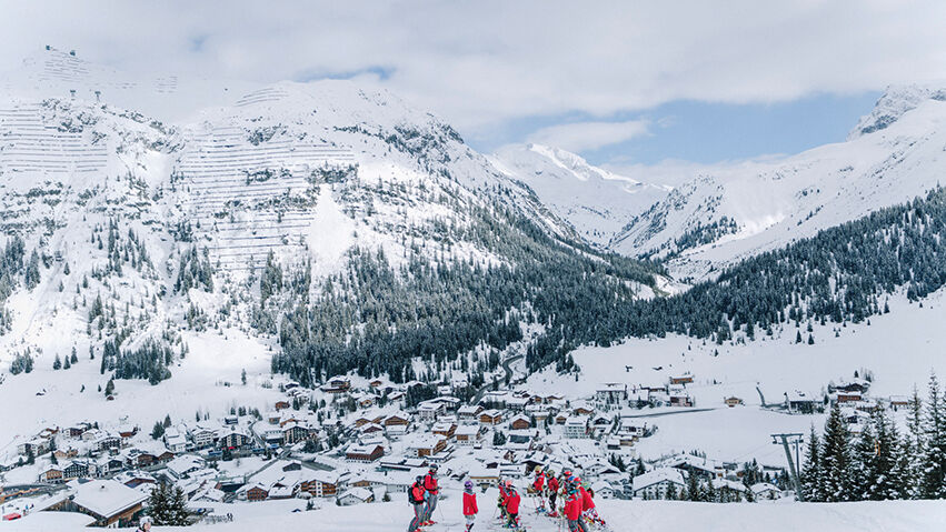mehrere Personen des Skiclubs genießen die traumhafte Aussicht auf Lech und die verschneite Bergkulisse im Hintergrund