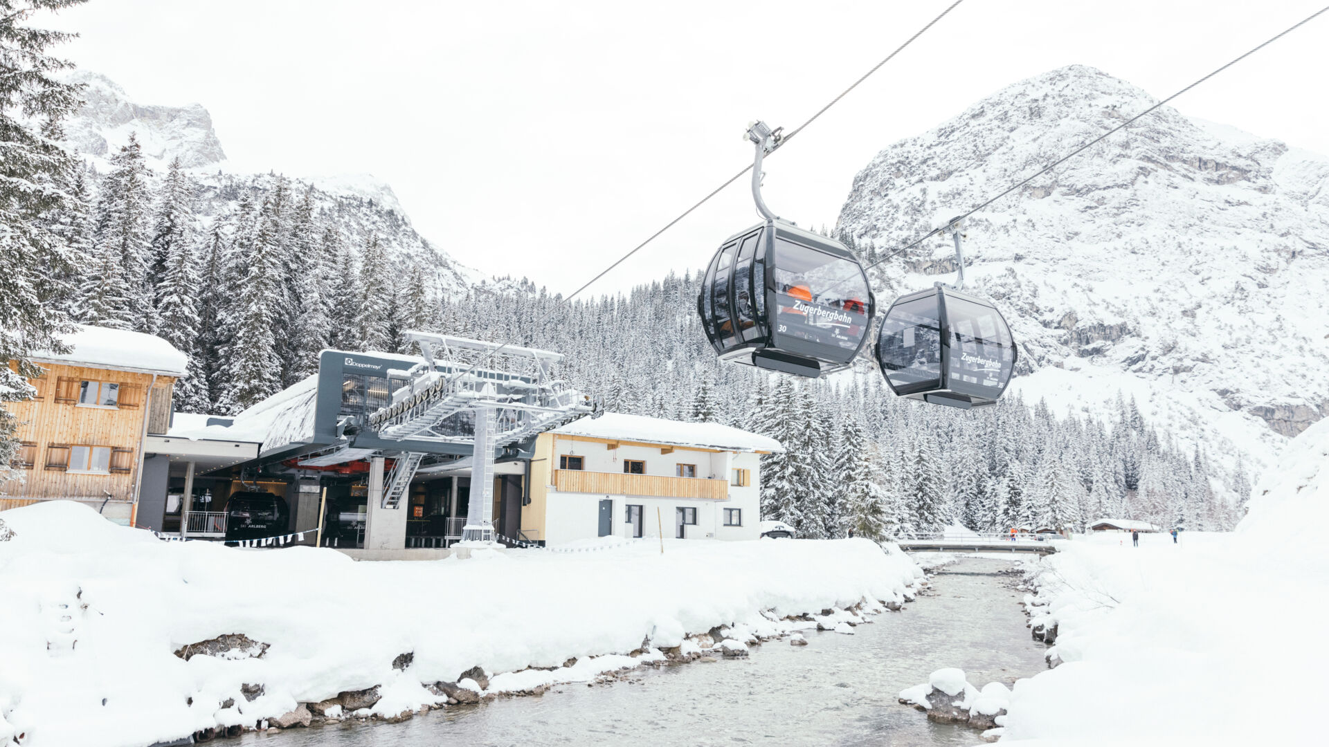 die Talstation der Zugerbahn, die Bahn fährt über die verschneite Landschaft in Zug und über den Fluss Lech