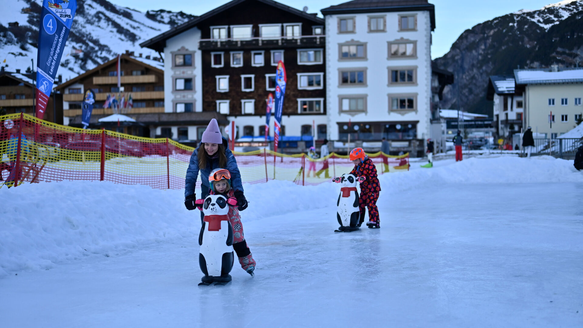 zwei Kinder fahren mit einer Eislaufhilfe Schlittschuhe auf dem Eislaufplatz in Zürs