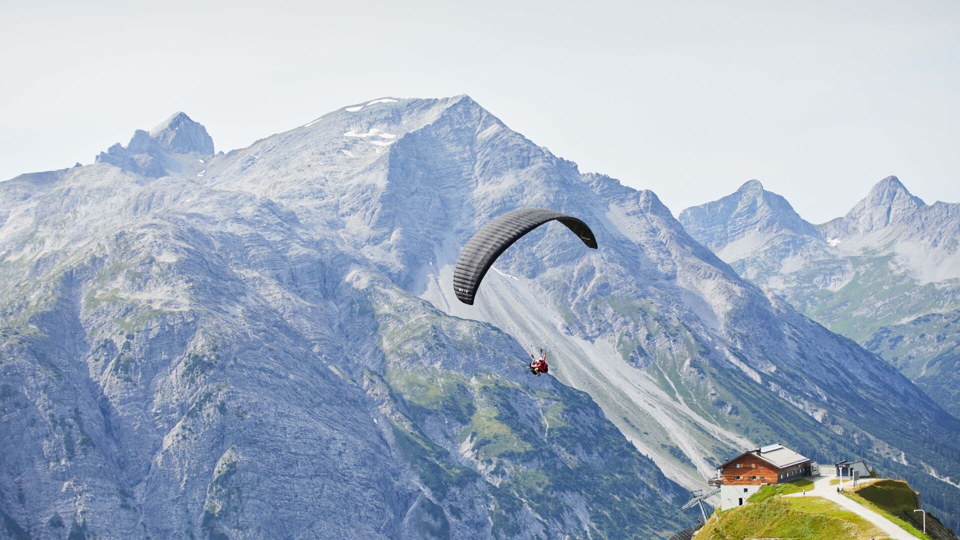 Ein Paragleiter von hinten zu sehen und im Hintergrund eine große weite zu sehen mit Berggipfeln