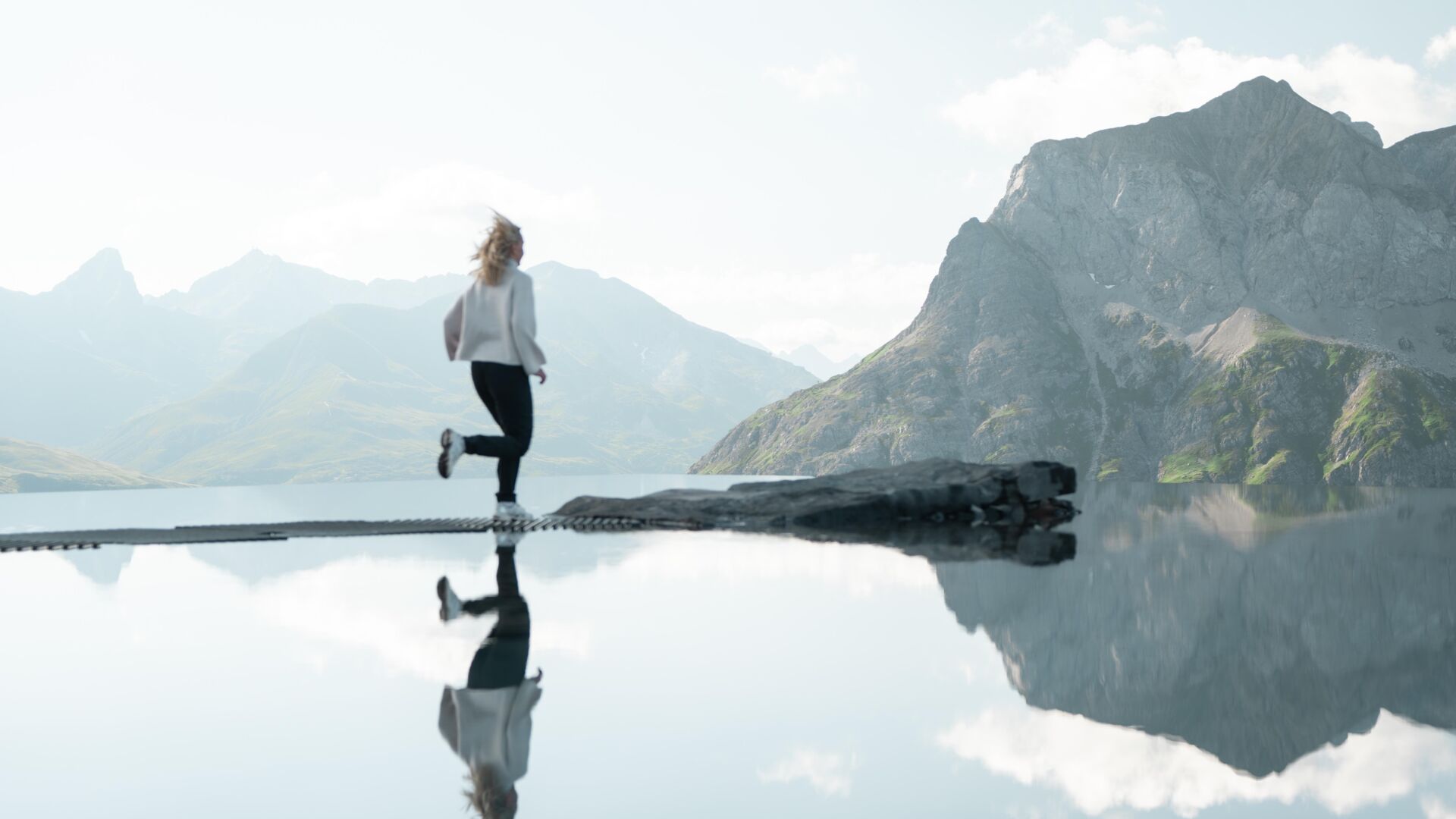 Frau auf Felsen in einem spiegelnden Bergsee vor schroffem Alpenpanorama.