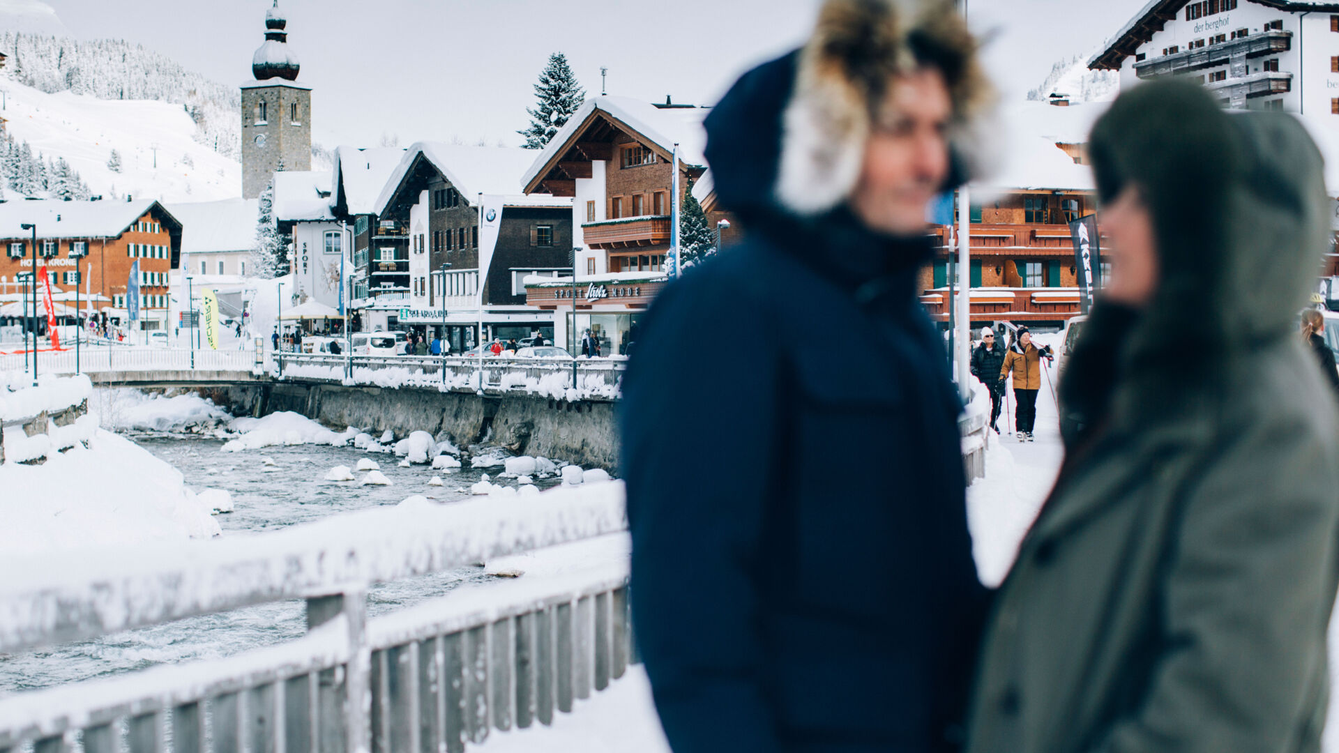 zwei Personen genießen einen ruhigen Moment zu Zweit beim Winterspaziergang durch das Dorf, während man im Hintergrund die schöne schneebedeckte Lechpromenade sieht
