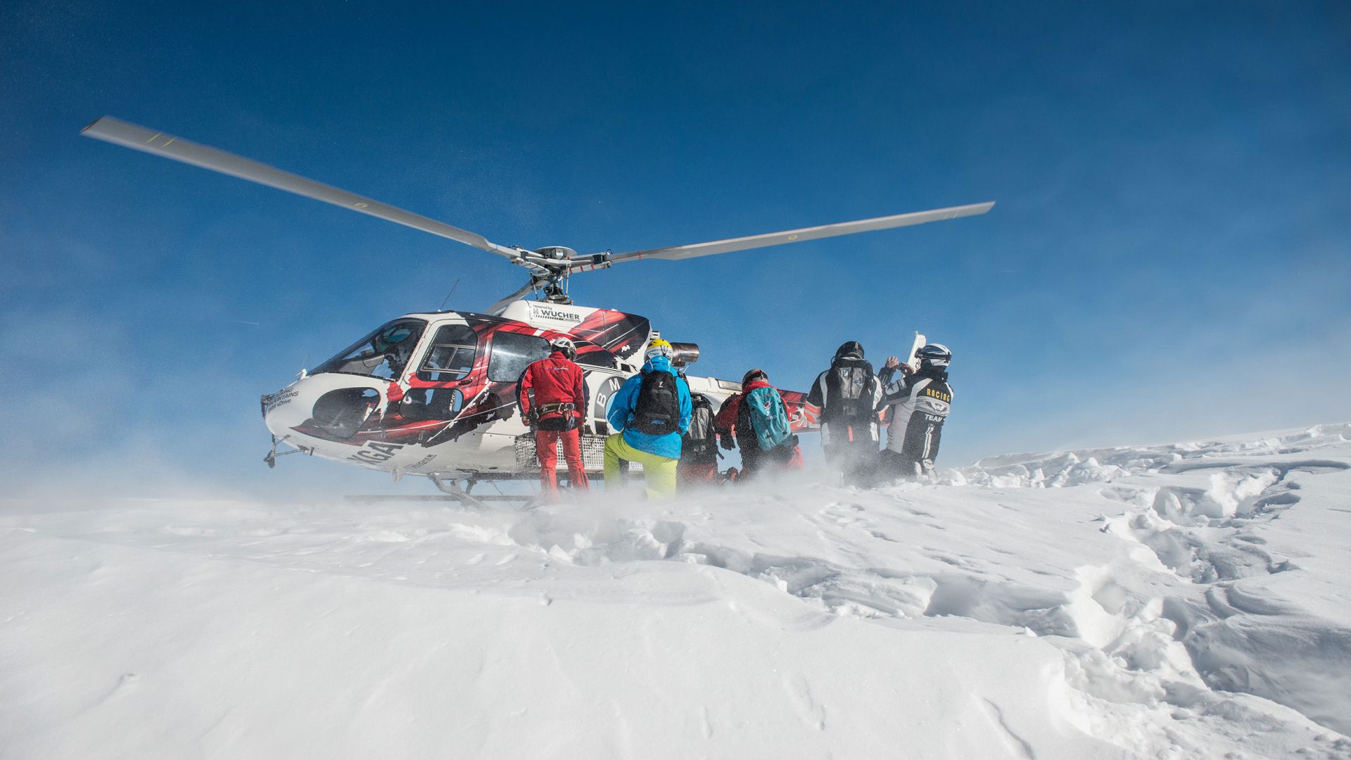Eine Gruppe von Freeridern steht vor dem gelandeten Hubschrauber inmitten von frischem Pulverschnee