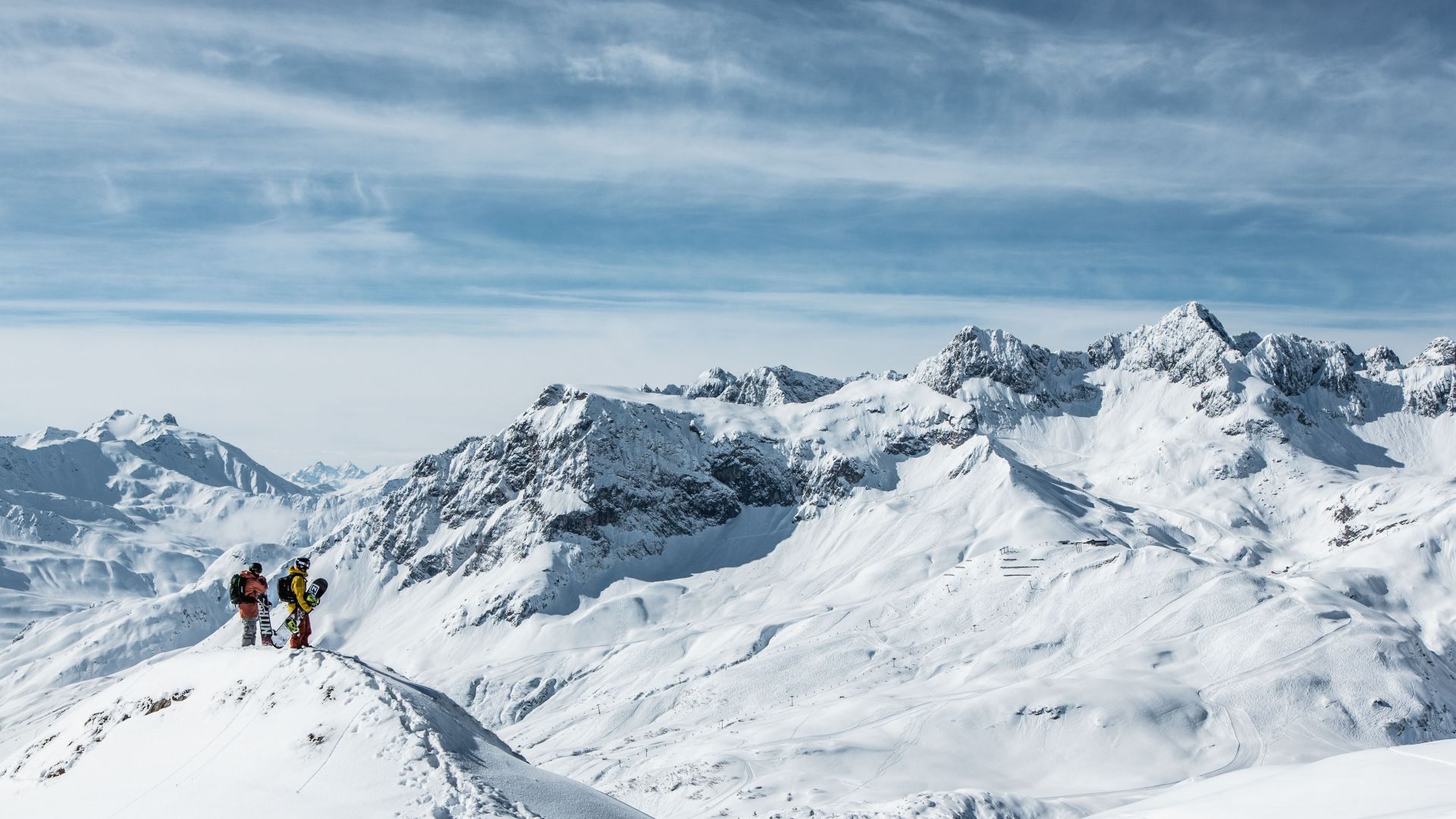 zwei Snowboarder stehen am Tiefschneehang und genießen die traumhafte Aussicht auf die verschneite Bergkulisse von Lech Zürs am Arlberg