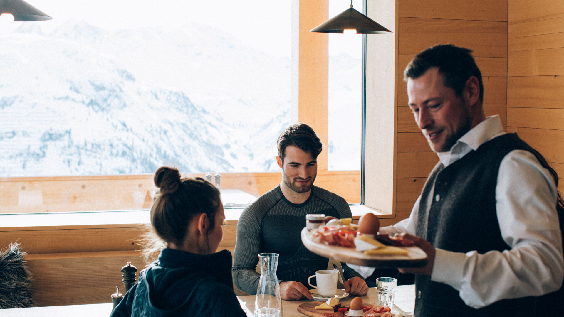 Ein Kellner bringt eine Frühstücksplatte zu den Gästen an den Tisch
