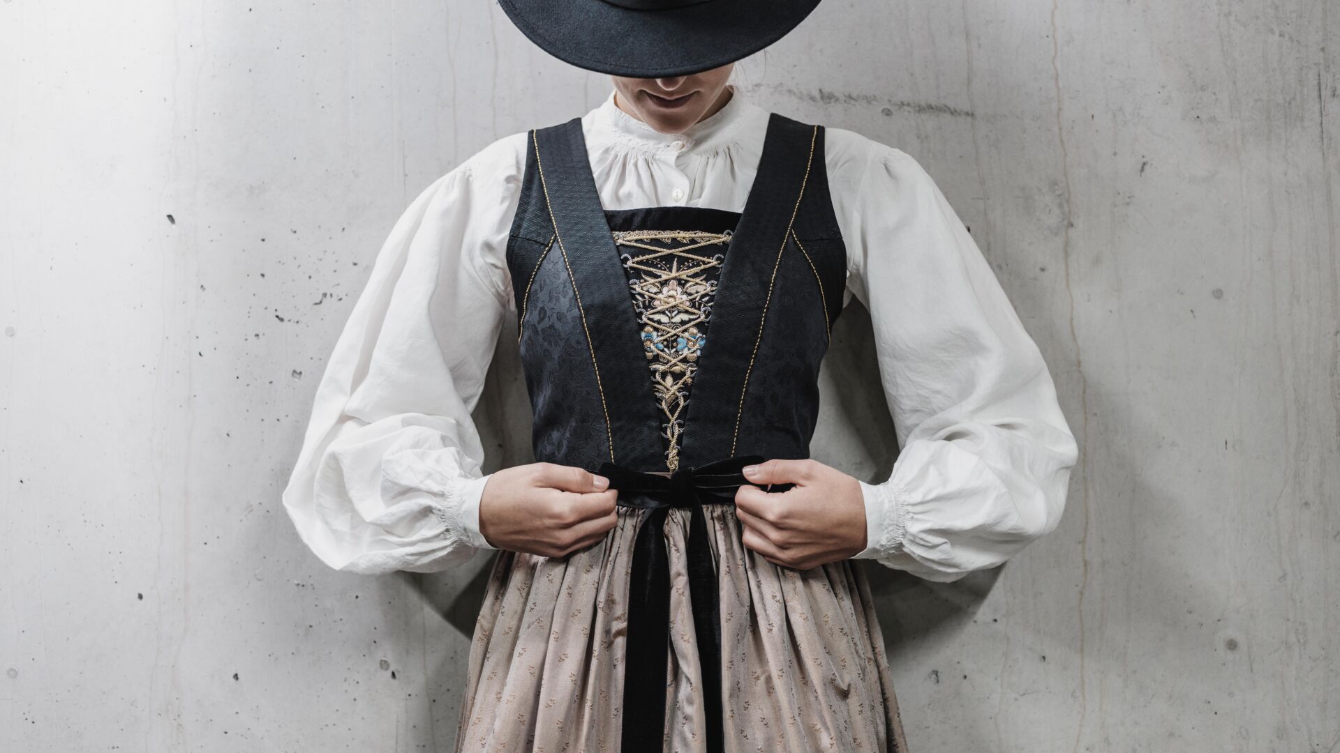 Frau in Walser Tracht mit schwarzen Wollrock, verziertem Mieder, Schürze und schwarzen Hut