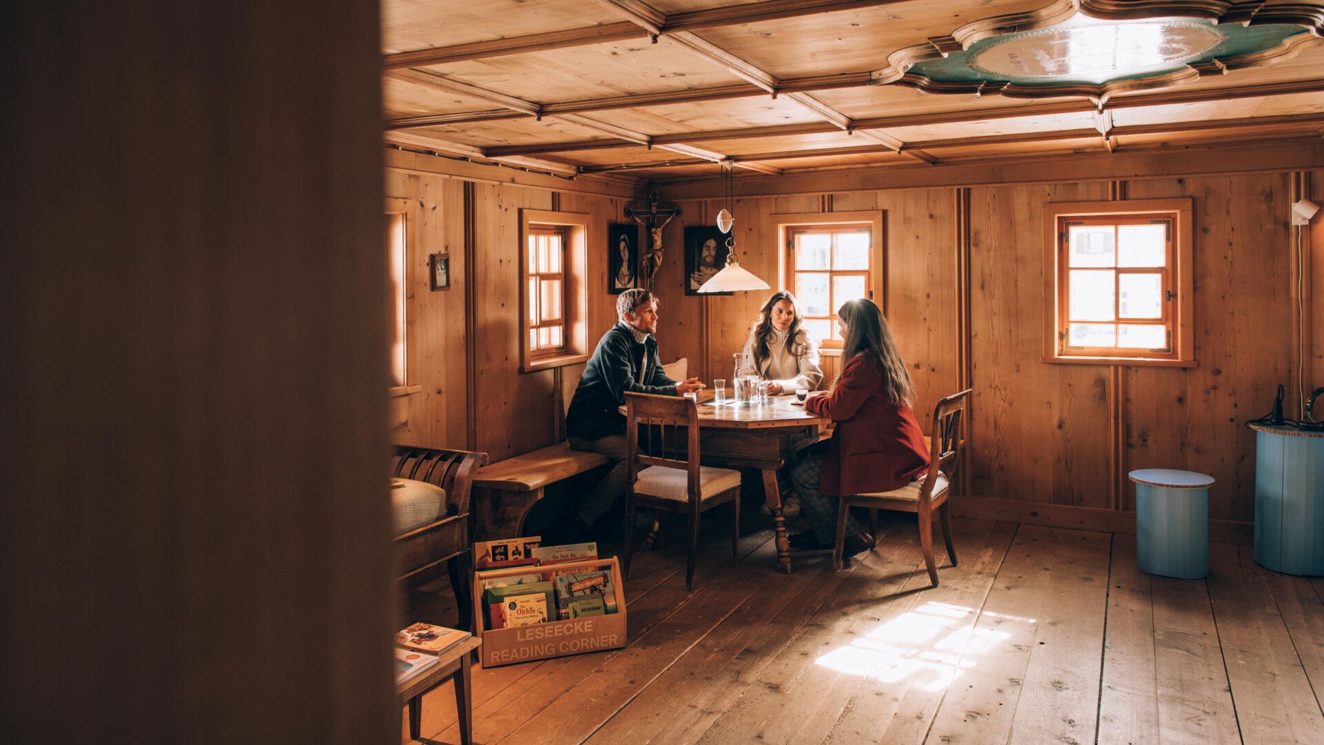 drei Personen sitzen an einem runden Tisch im Huber-Hus, in einem gemütlichen, urigen Ambiente
