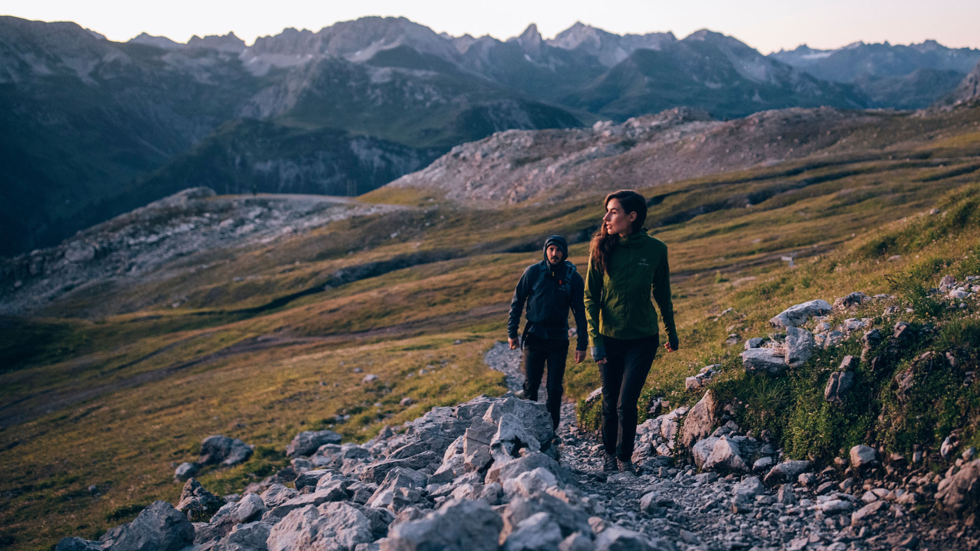Eine Frau und ein Mann wandern auf einem Steig im Hochgebirge bei Sonnenaufgang