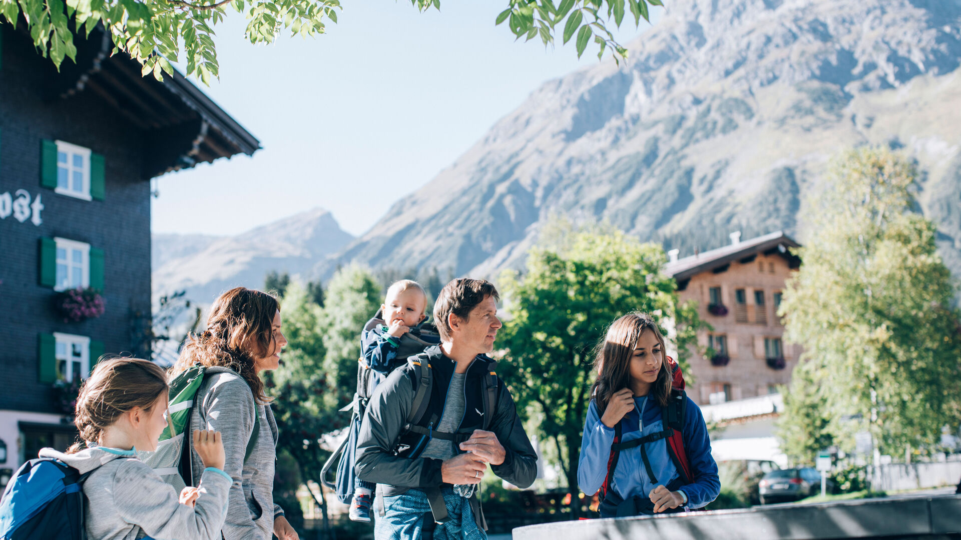 eine Familie steht vor dem Dorfbrunnen in Lech, im Hintergrund sieht man das Omeshorn