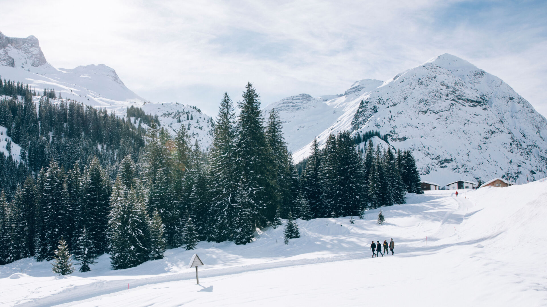 Blick auf den Winterwanderweg, der neben den verschneiten Nadelbäumen und den winterlichen Bergkulissen entlang geht