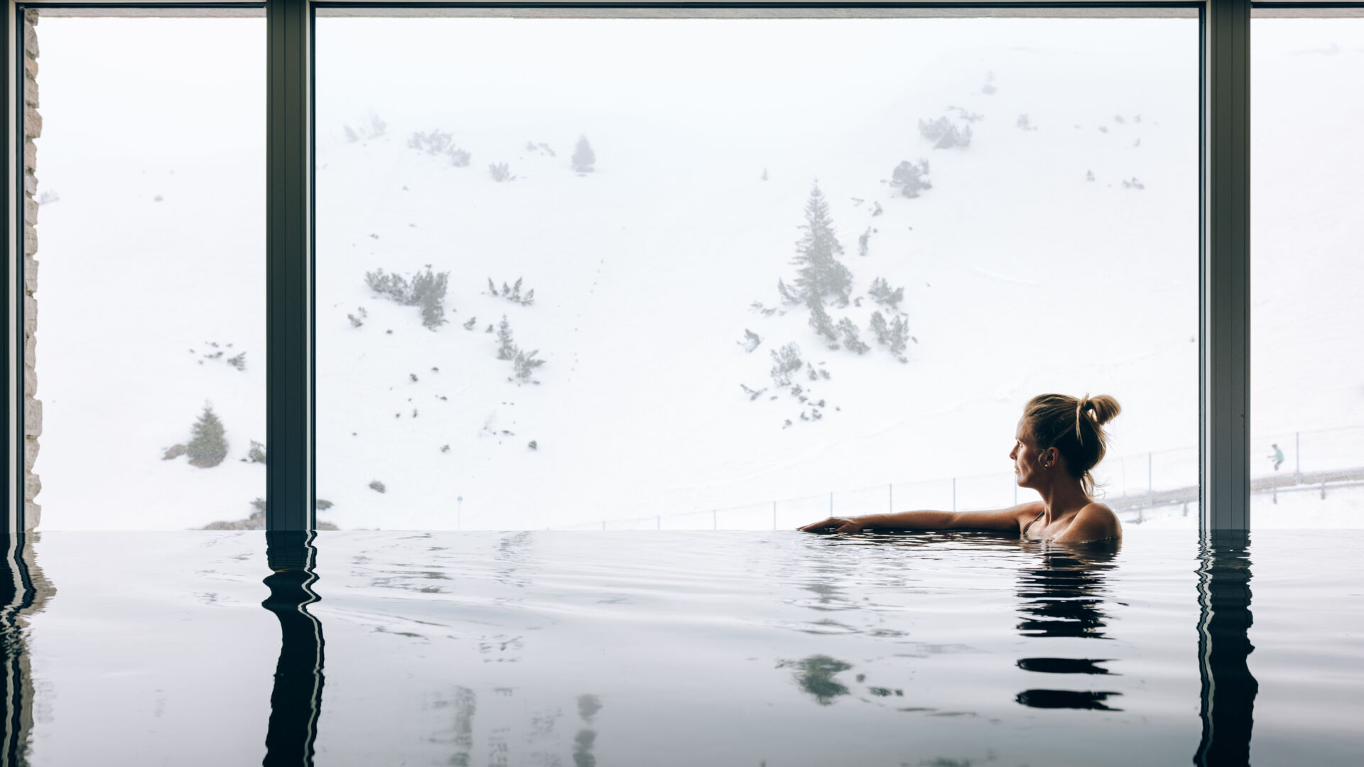 eine Frau genießt die winterliche Aussicht im Infinity Pool des Zürserhof mit Panoramablick auf Zürs