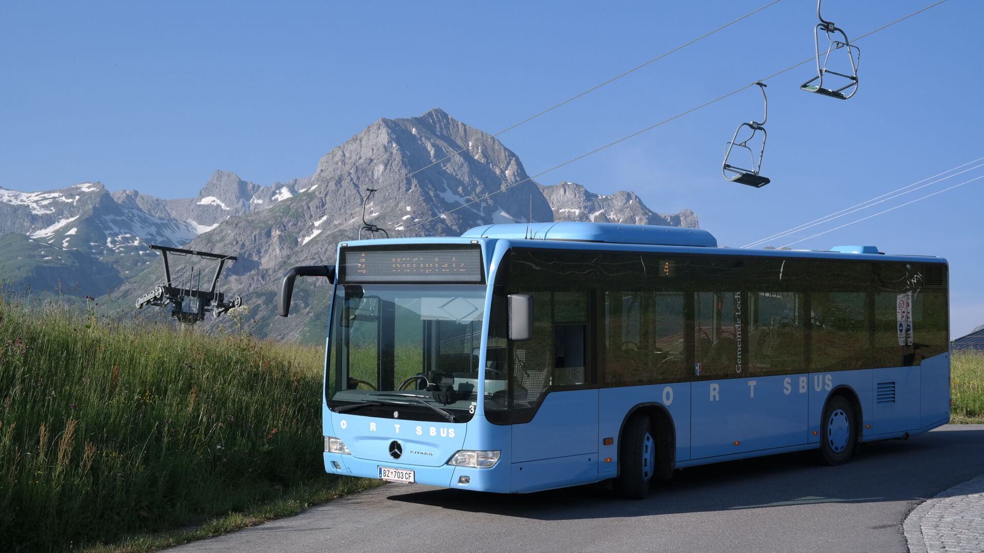 Im Vordergrund ist der blaue Ortsbus zu sehen und im Hintergrund das Omeshorn mit dem 2er Sessellift der Schlosskopfbahn