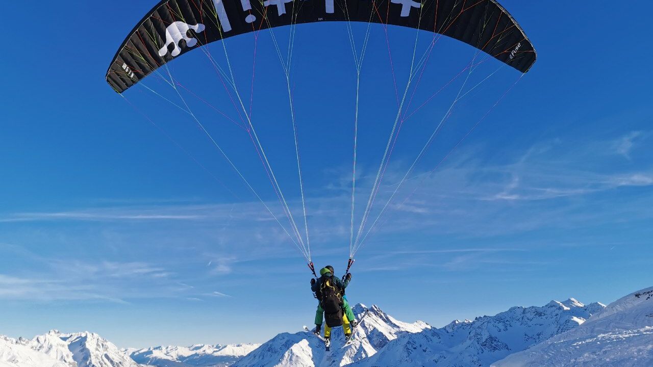 Gleitschirm mit Tandemflug zu sehen von hinten hängen zwei Personen am Gleitschirm und im Hintergrund ist die Berglandschaft zu sehen