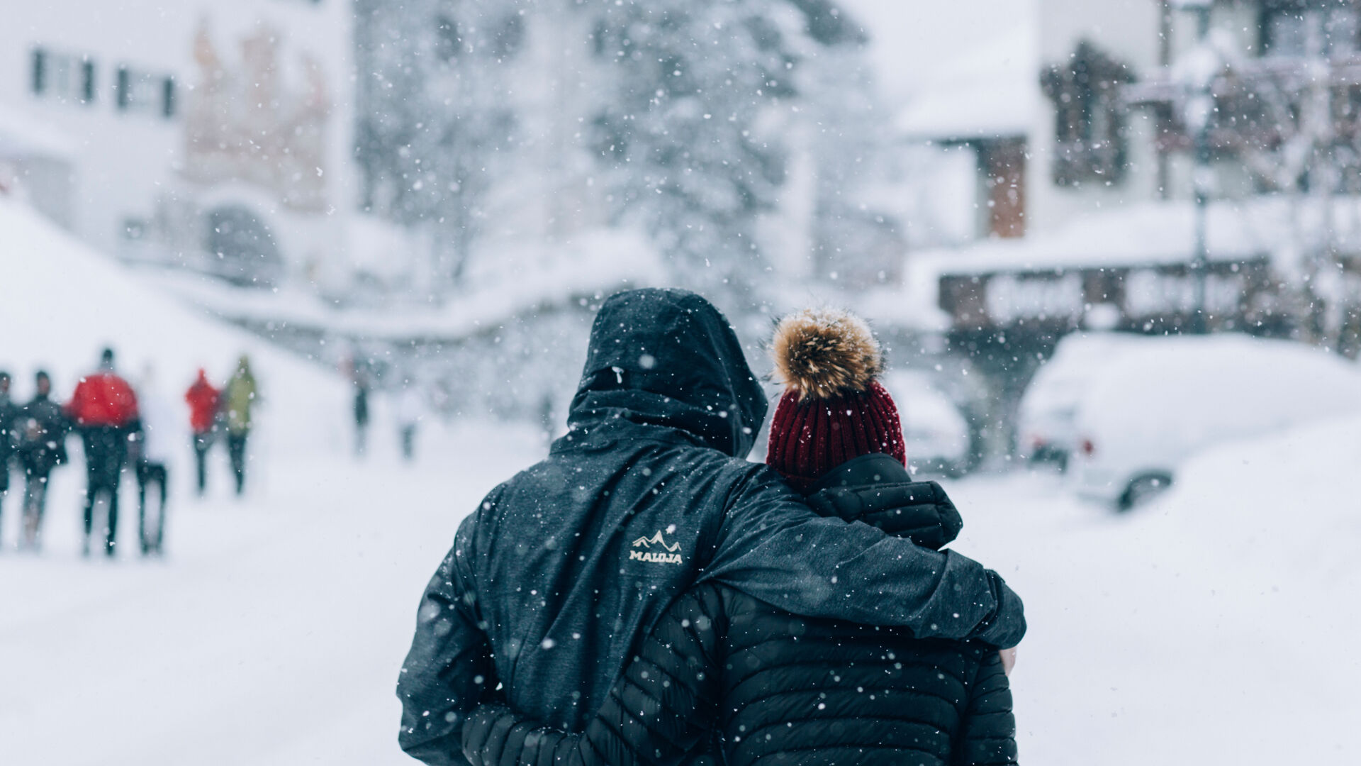 zwei Personen laufen Hand in Hand durch den Schnee im Dorfzentrum von Lech während es gerade schneit