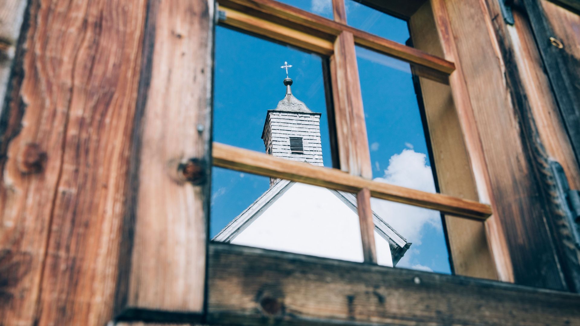 die Kirche von Bürstegg spiegelt sich in einem urigen Fenster wieder 