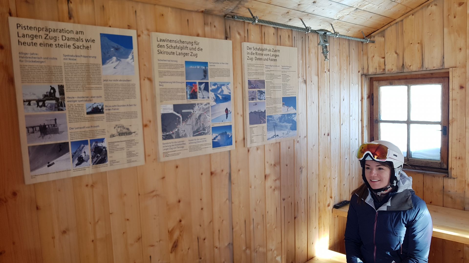 eine Skifahrerin sitzt im Infopoint langer Zug, wo verschiedene Informationsflyer auf der Wand hängen