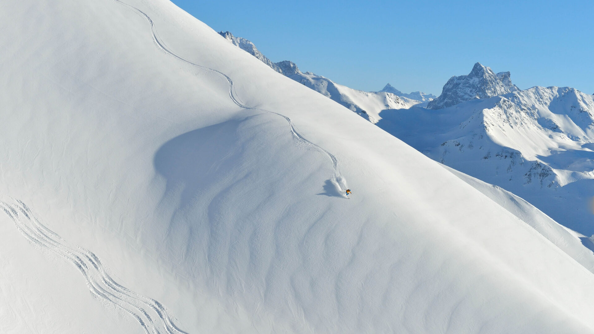 Skifahrer fährt einen offenen weiten weiß verschneiten Hang hinab und zieht die erste Line