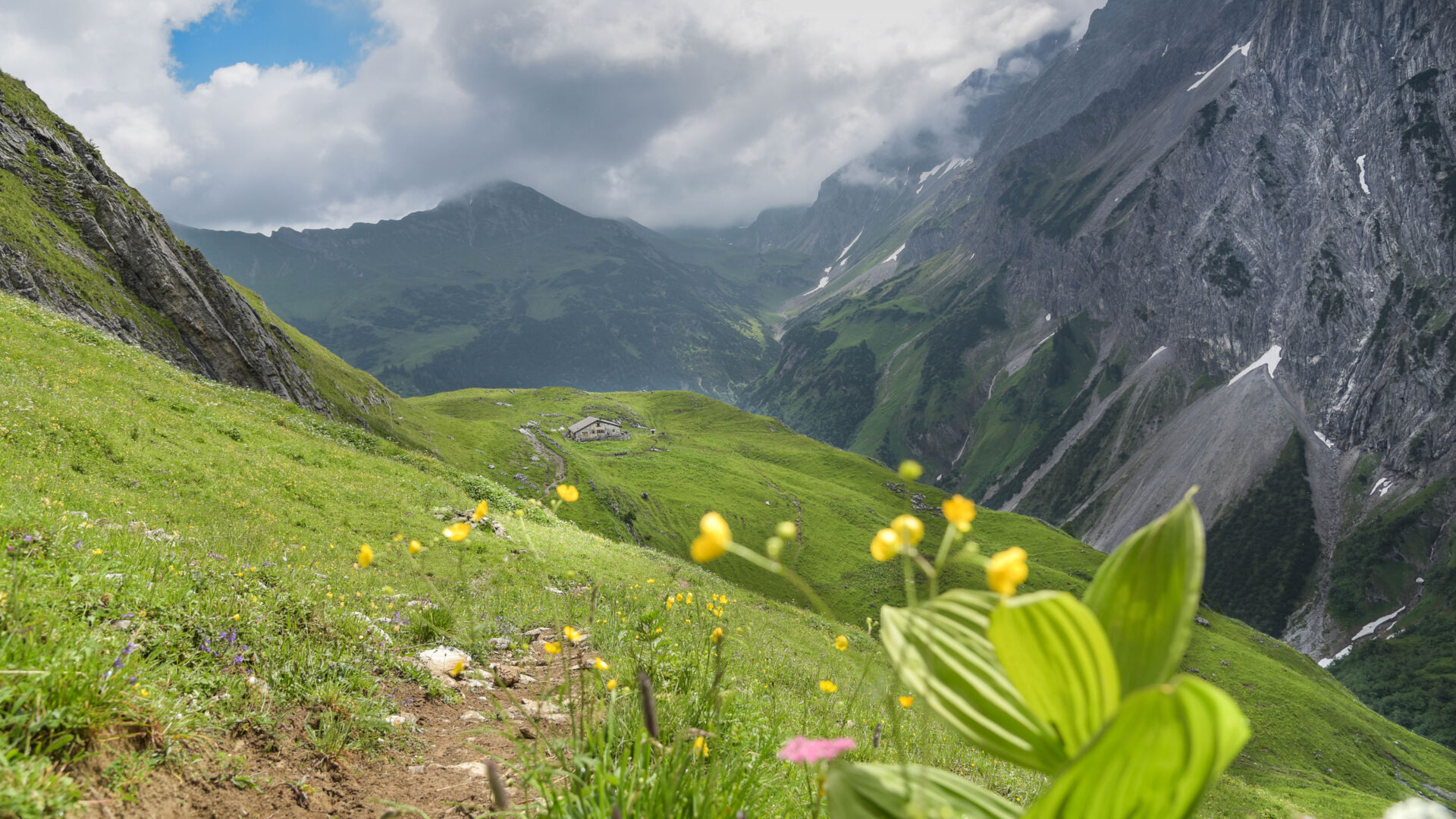 Satte grüne Wiesen und ein Bergpanorama das von dunklen Wolken getrübt wird
