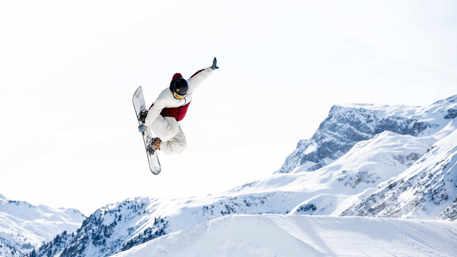 Freestyler springt über eine Schanze und im Hintergrund ist strahlend blauer Himmel und eine wunderschöne Bergkulisse zu sehen.