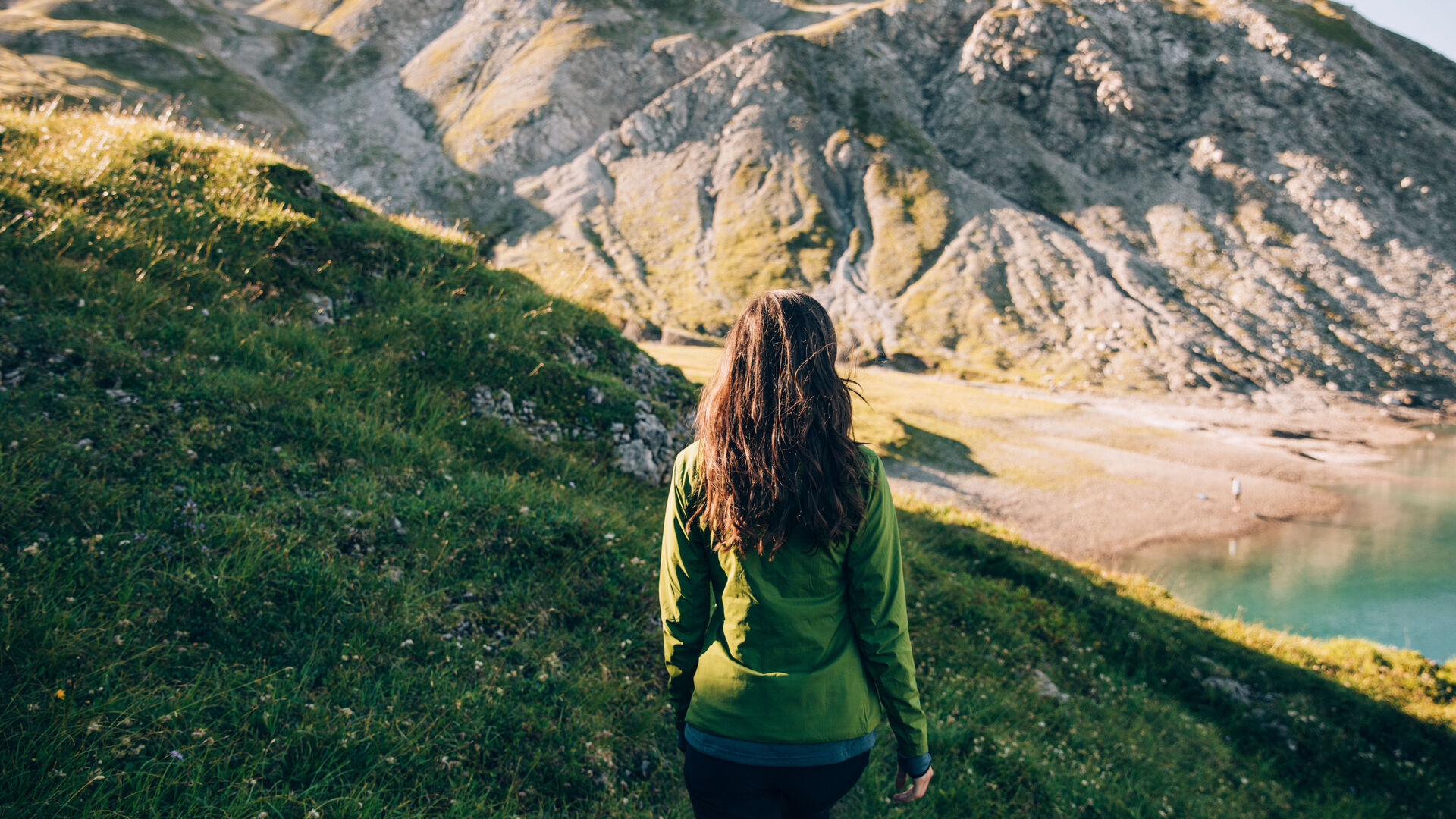 Wanderin steht auf Gebirgshang und schaut in Richtung des türkisen Butzensees umringt von einer imposanten Gebirgslandschaft