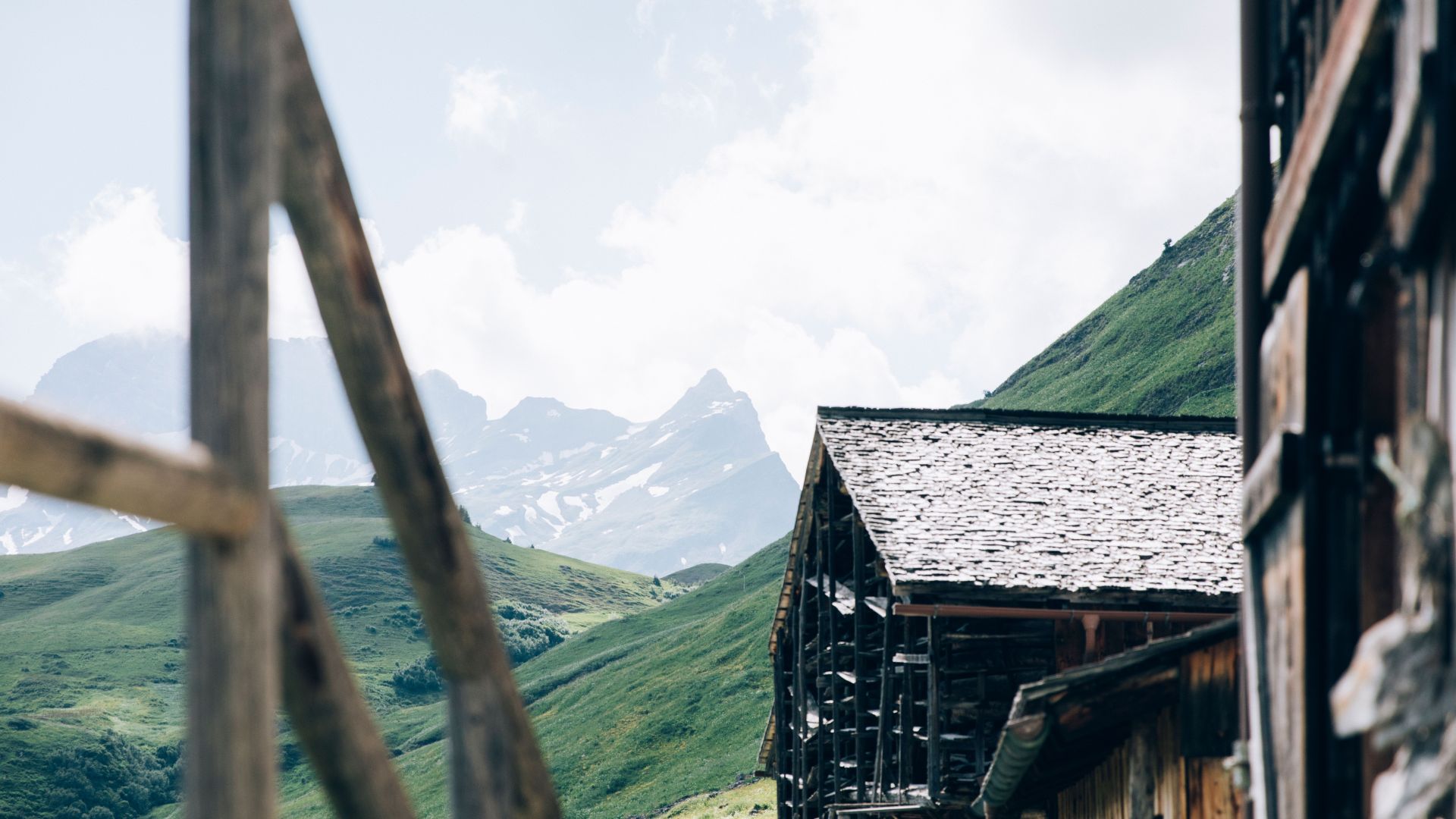 Blick von einer Terrasse auf ein anderes uriges Holzhaus in Bürstegg, im Hintergrund sieht man das Bergpanorama