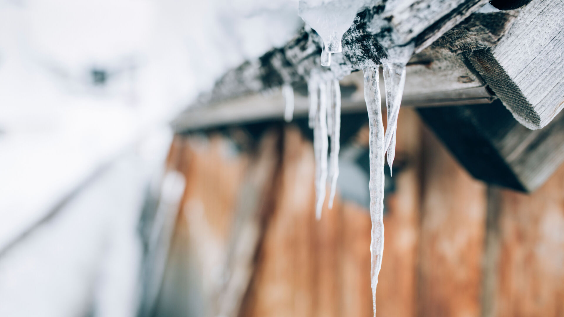 einige Eiszapfen hängen von einem schneebedeckten Holzdach