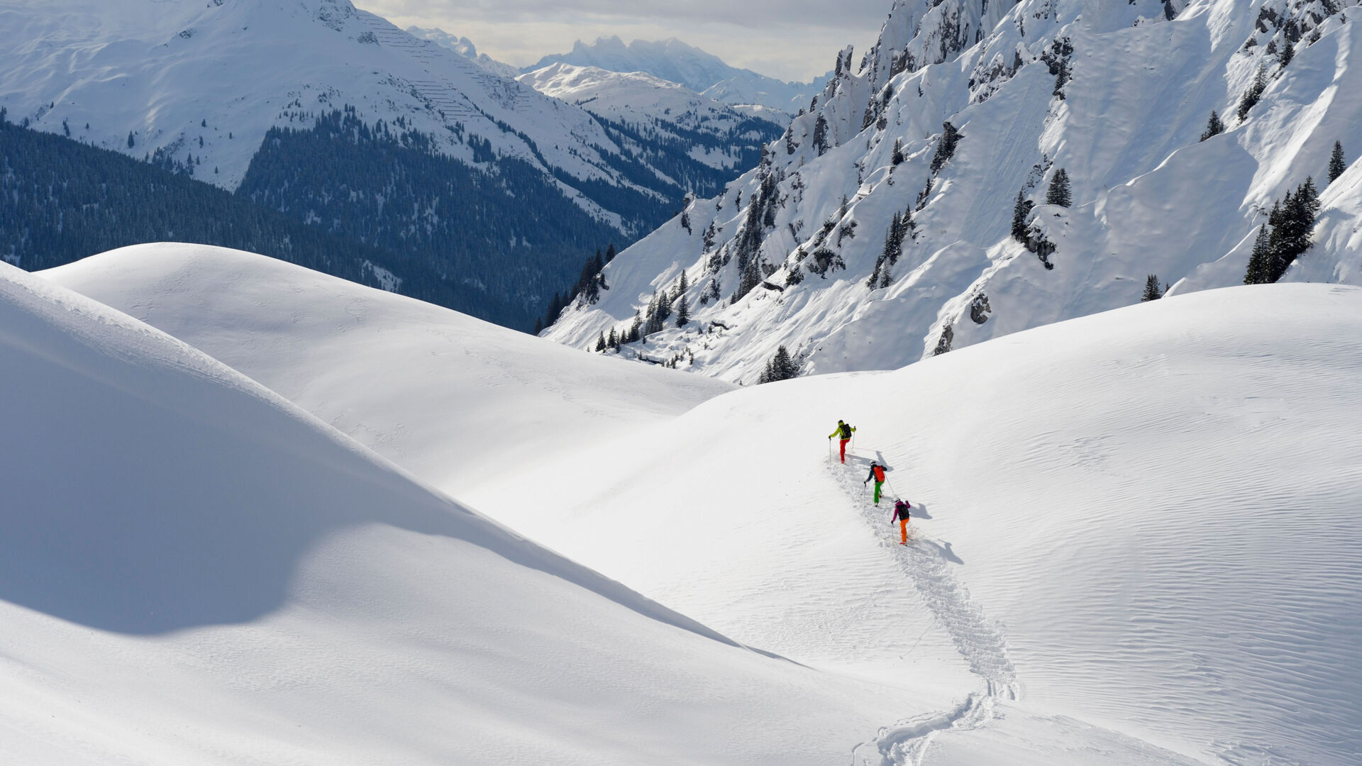 Drei Skifahrer stapfen im Gelände den Tiefschneehang hinauf für die nächste Abfahrt