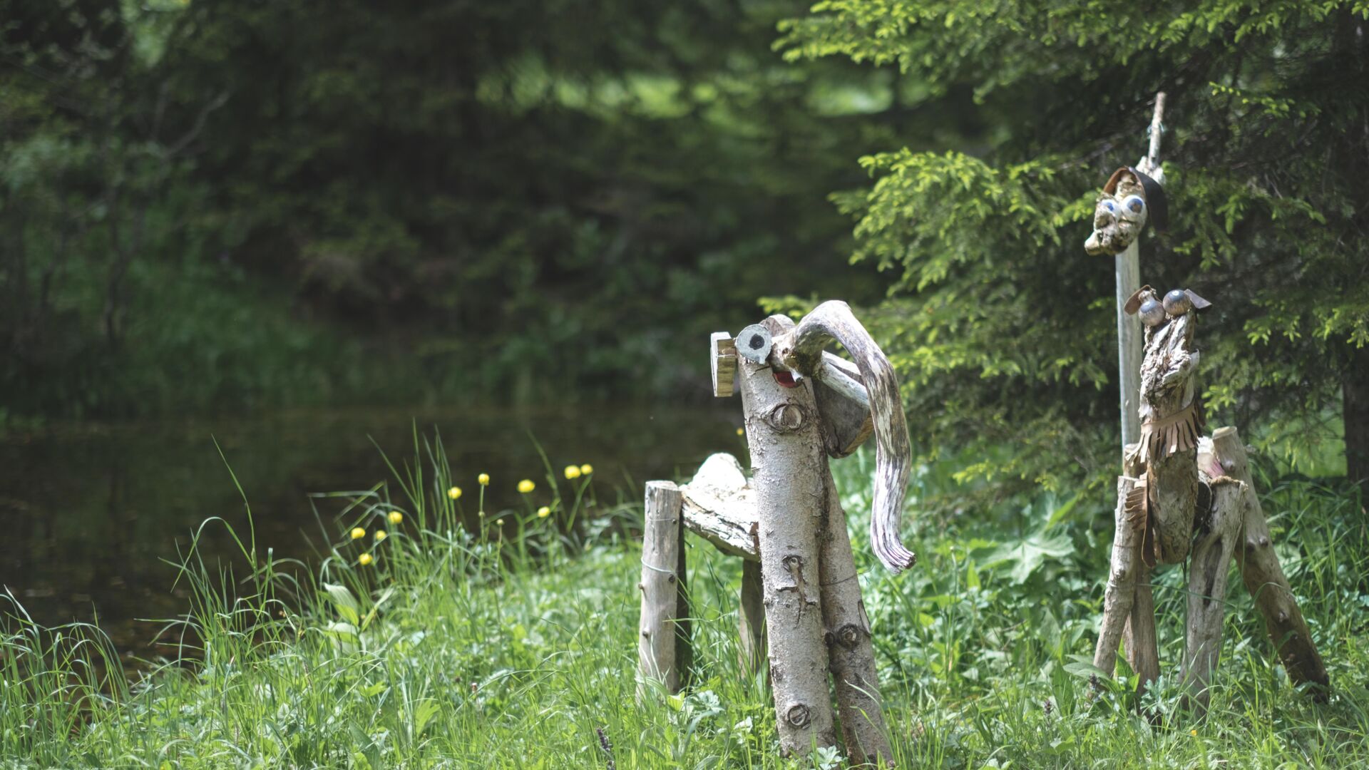 Zwei Holzfiguren stehen in einer Wiese im Wald