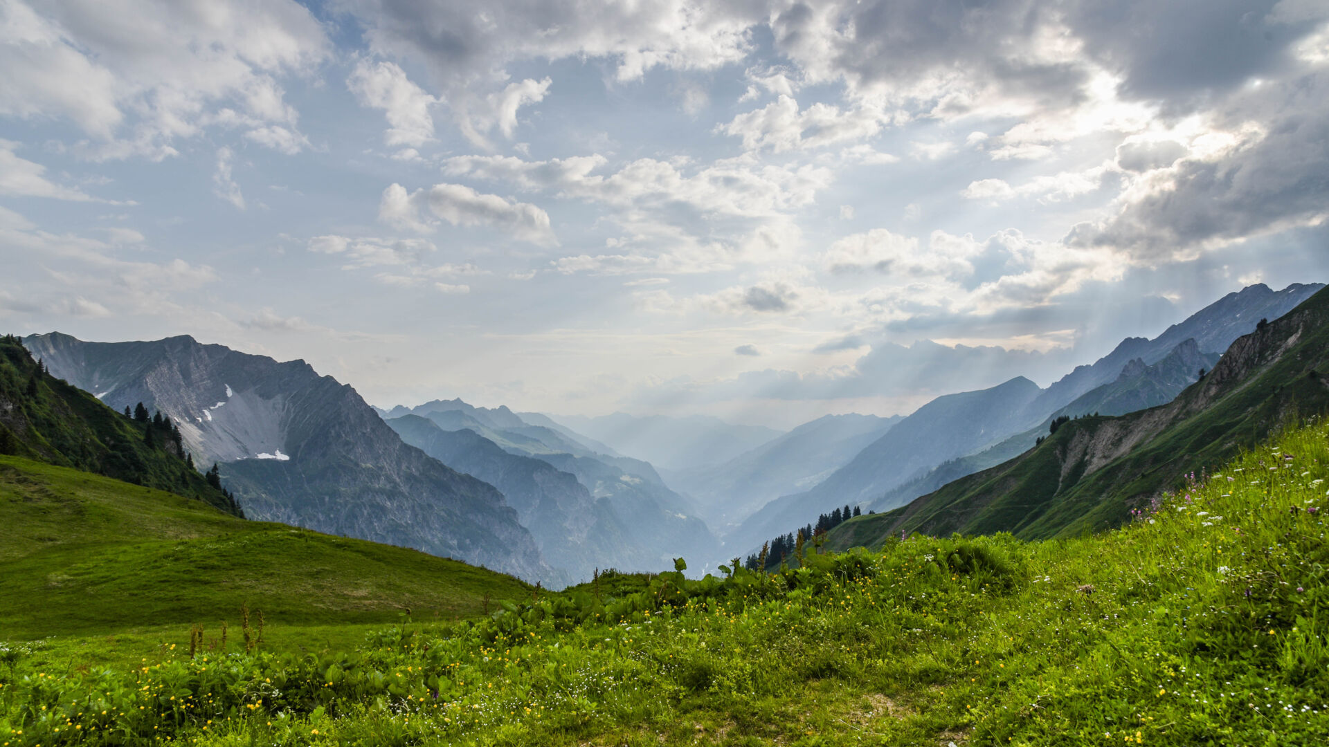 Das Sonnenlicht fällt durch die Wolkendecke, im Gebirge, satte gruene Wiesen und ein schoenes Bergpanorama
