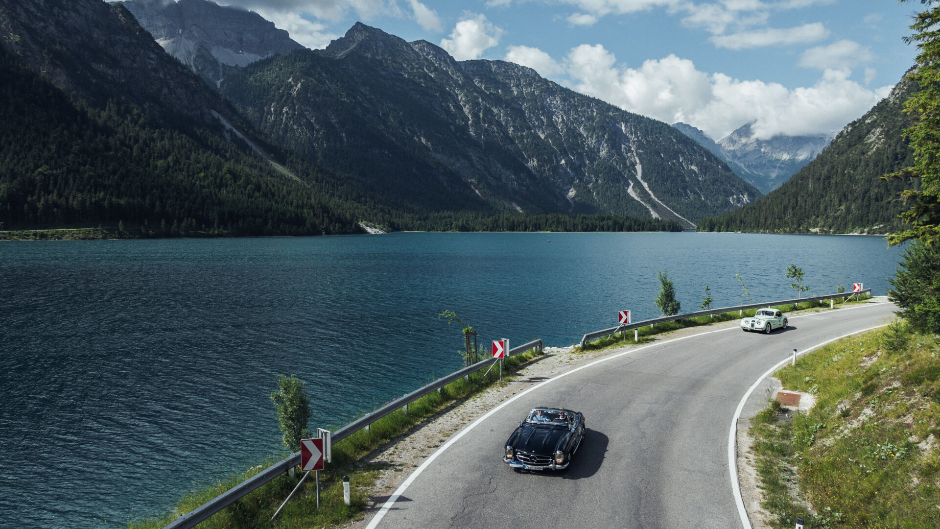 Oldtimer fährt in bergiger Landschaft mit blauen See im Hintergrund