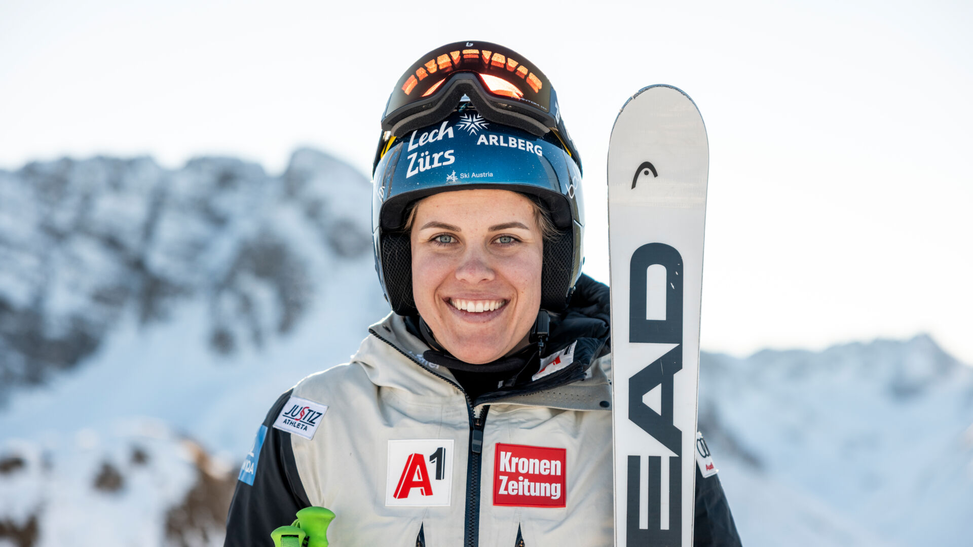 Eine lachende Person Magdalena Egger im Bild mit Skihelm am Kopf und Lech Zürs Logo auf der Vorderseite zu sehen. Sie hält die HEAD Ski in den Händen