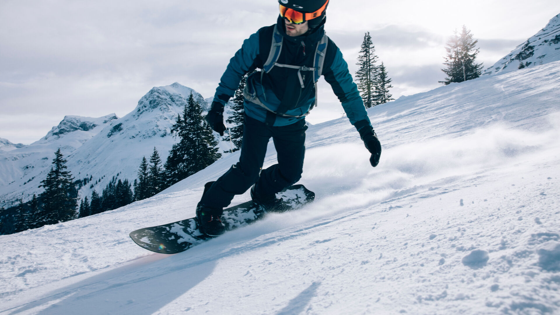 ein Snowboarder fährt über die frisch präparierte Piste bei traumhaftem Wetter, im Hintergrund sieht man das winterliche Bergpanorama