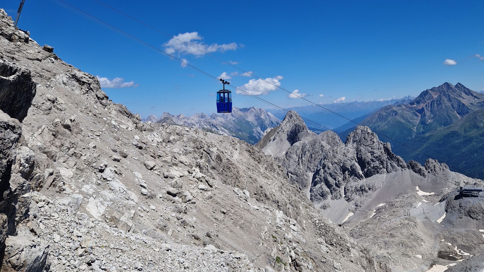 eine Gondel fährt über die felsige Berglandschaft, im Hintergrund sieht man das Bergpanorama