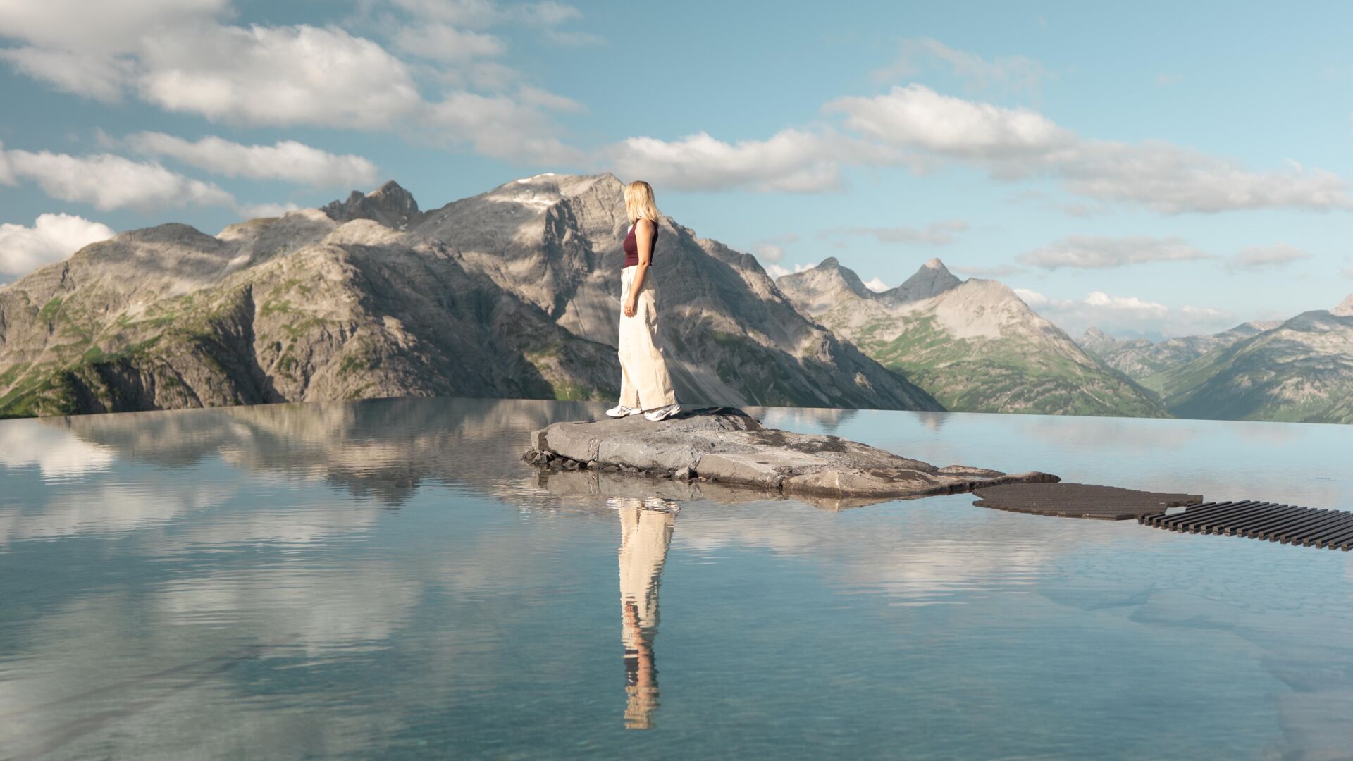 Frau auf Felsen in einem spiegelnden Bergsee vor schroffem Alpenpanorama.