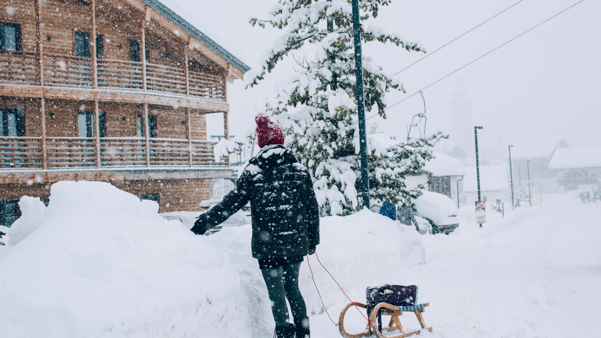 eine Person steht mit ihrem Rodel auf der schneebedeckten Straße während es gerade schneit
