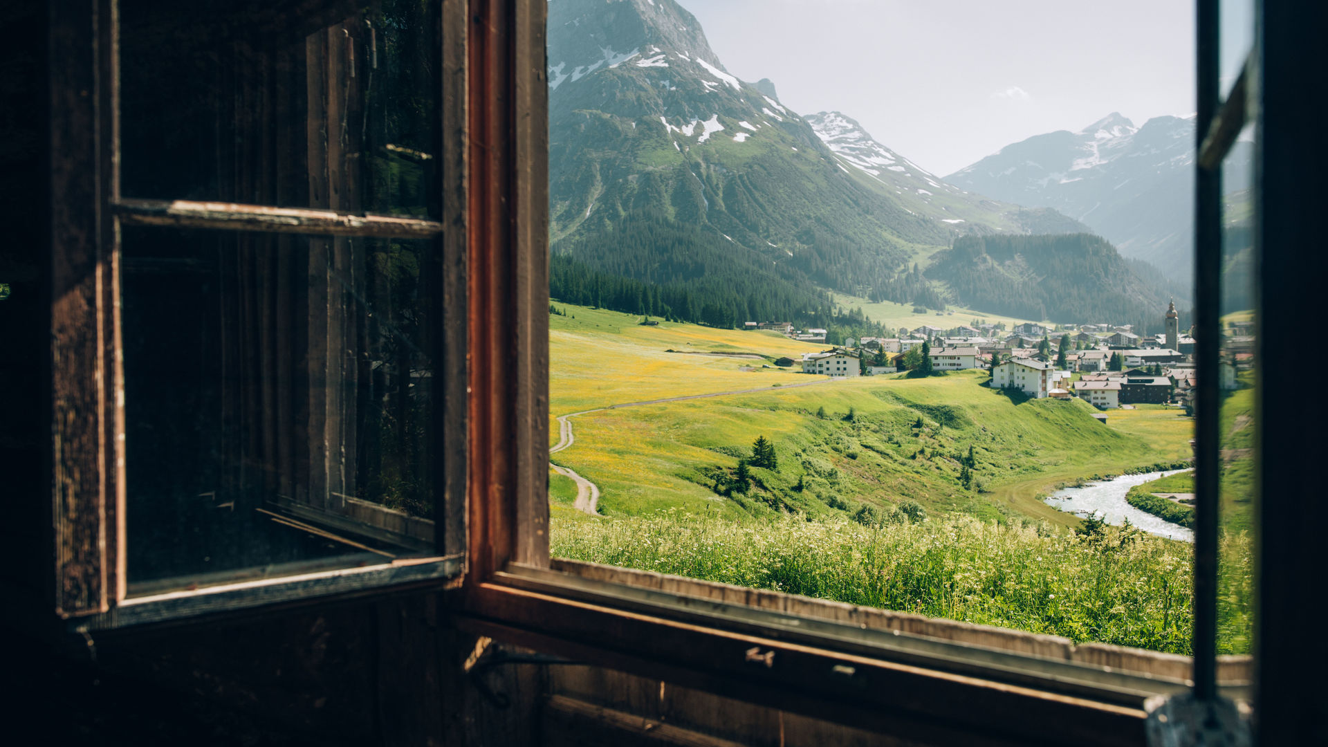 Blick aus einem rustikalen Fenster auf Lech und das Omeshorn im Frühling
