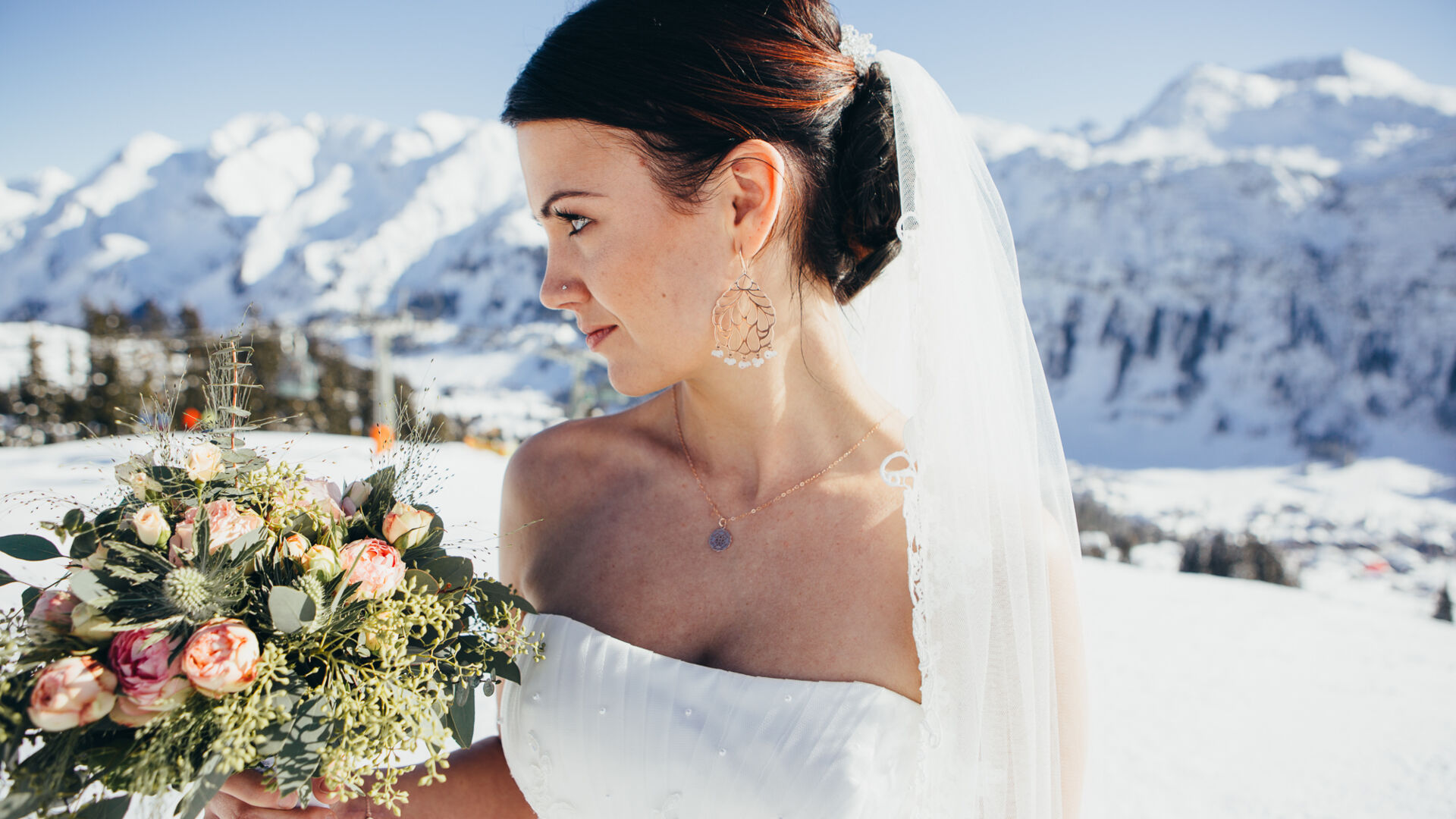 Die Braut hält ihren Hochzeitsstrauß und steht vor der winterlichen Bergkulisse bei ihrer Winterhochzeit am Arlberg